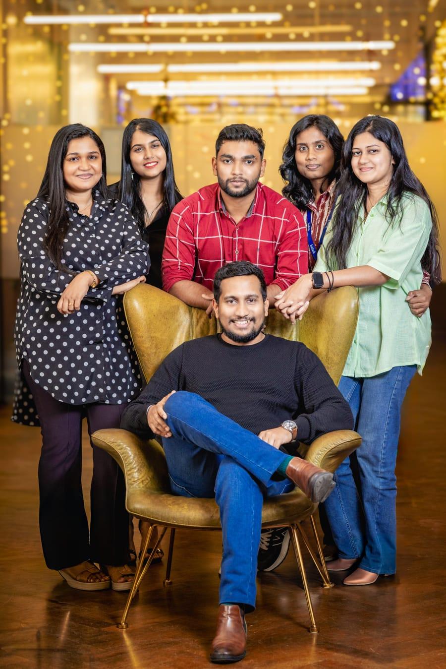 Six colleagues posing together around a leather armchair