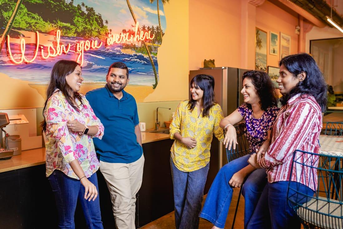 Five colleagues chatting by a counter beneath a beach mural