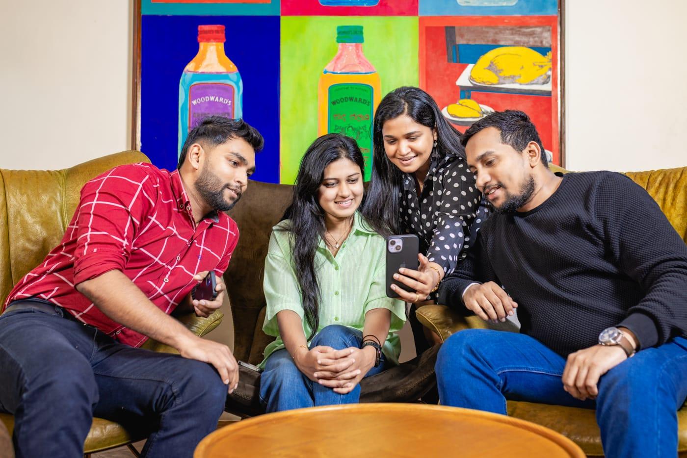 Four colleagues on a sofa, laughing at something on a phone