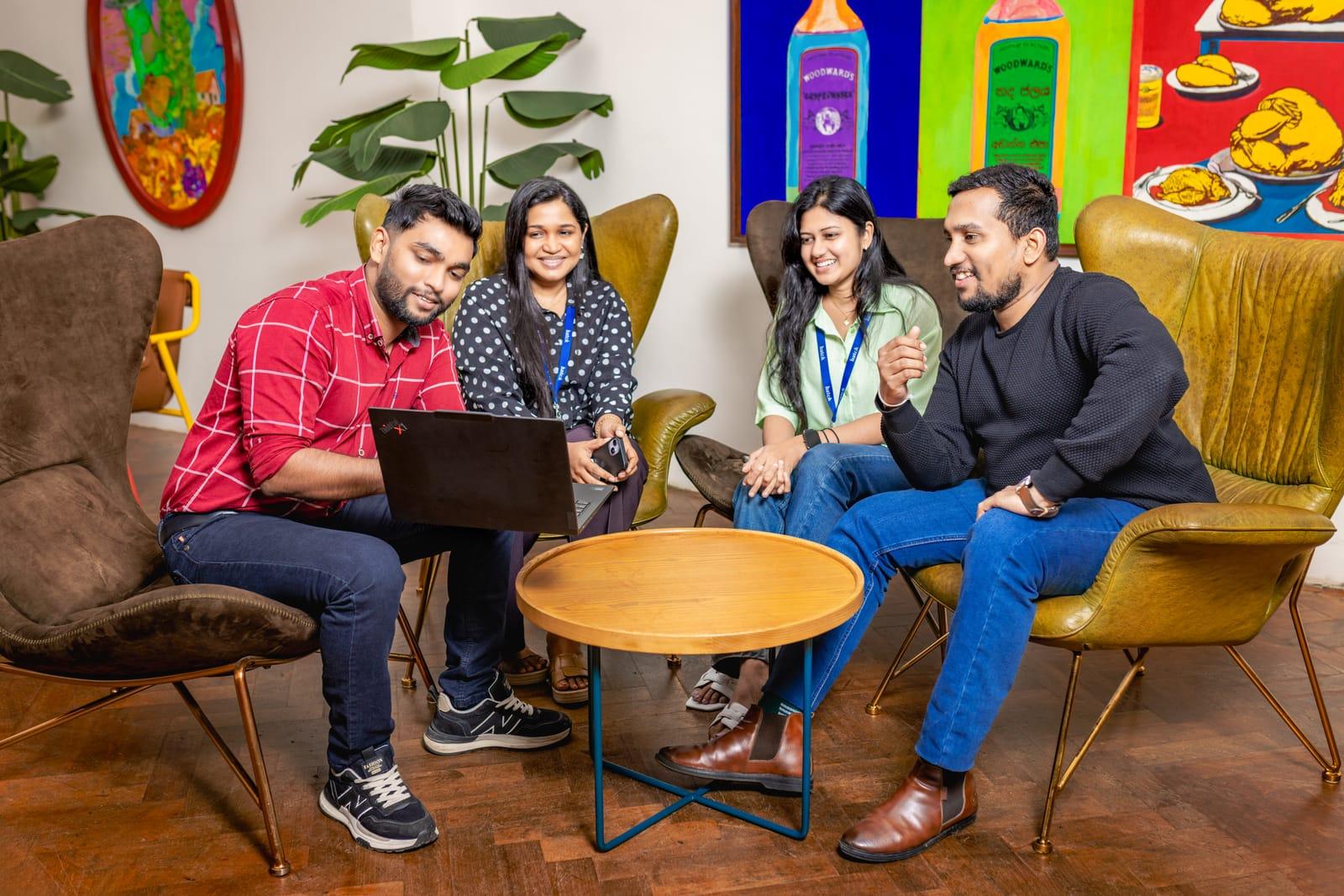Four colleagues in armchairs, working through something on a laptop